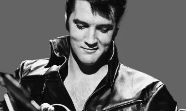 Elvis Presley strumming his guitar, captured in a timeless black and white photo, showcasing his iconic style and charm.